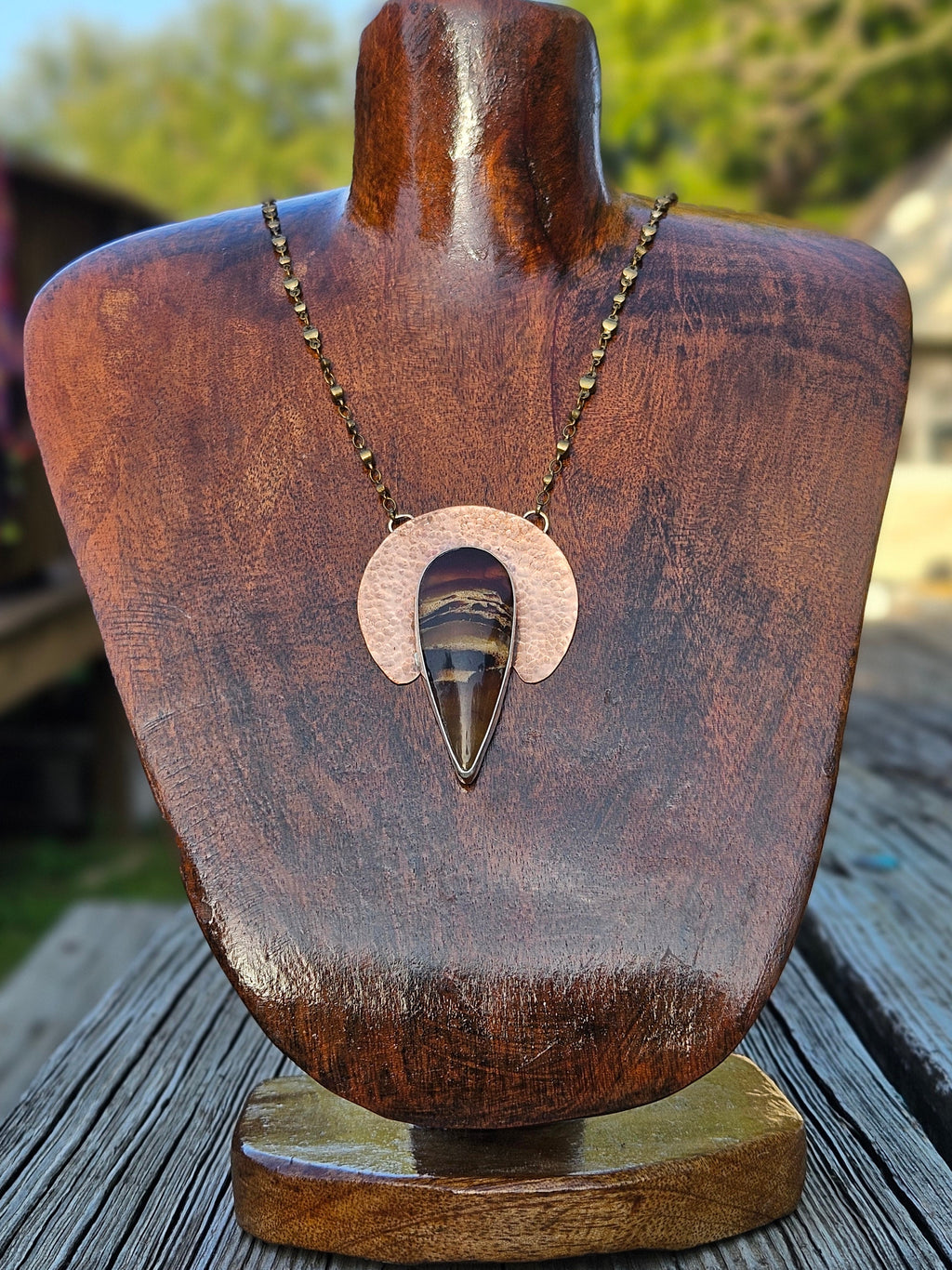Teardrop amber pendant with hammered crescent shape copper backplate with an amber piece set in sterling silver and a brass chain.