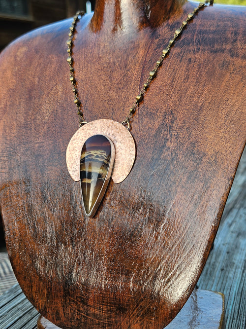 Teardrop amber pendant with hammered crescent shape copper backplate with an amber piece set in sterling silver and a brass chain.