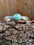 A sterling silver cuff bracelet with a round damele turquoise stone.