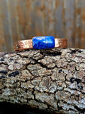 A hammered copper cuff with a rectangular blue lapis Lazuli set in the middle.