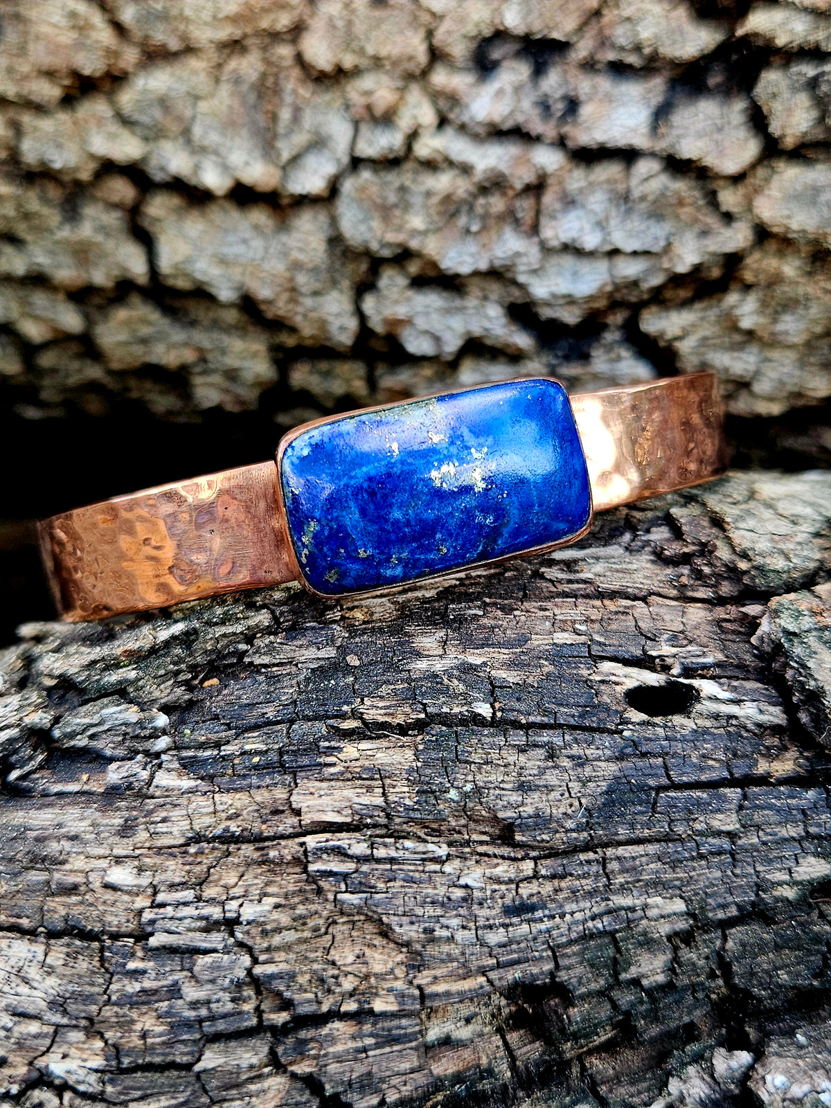 A hammered copper cuff bracelet with a rectangular blue lapis lazuli stone centerpiece.
