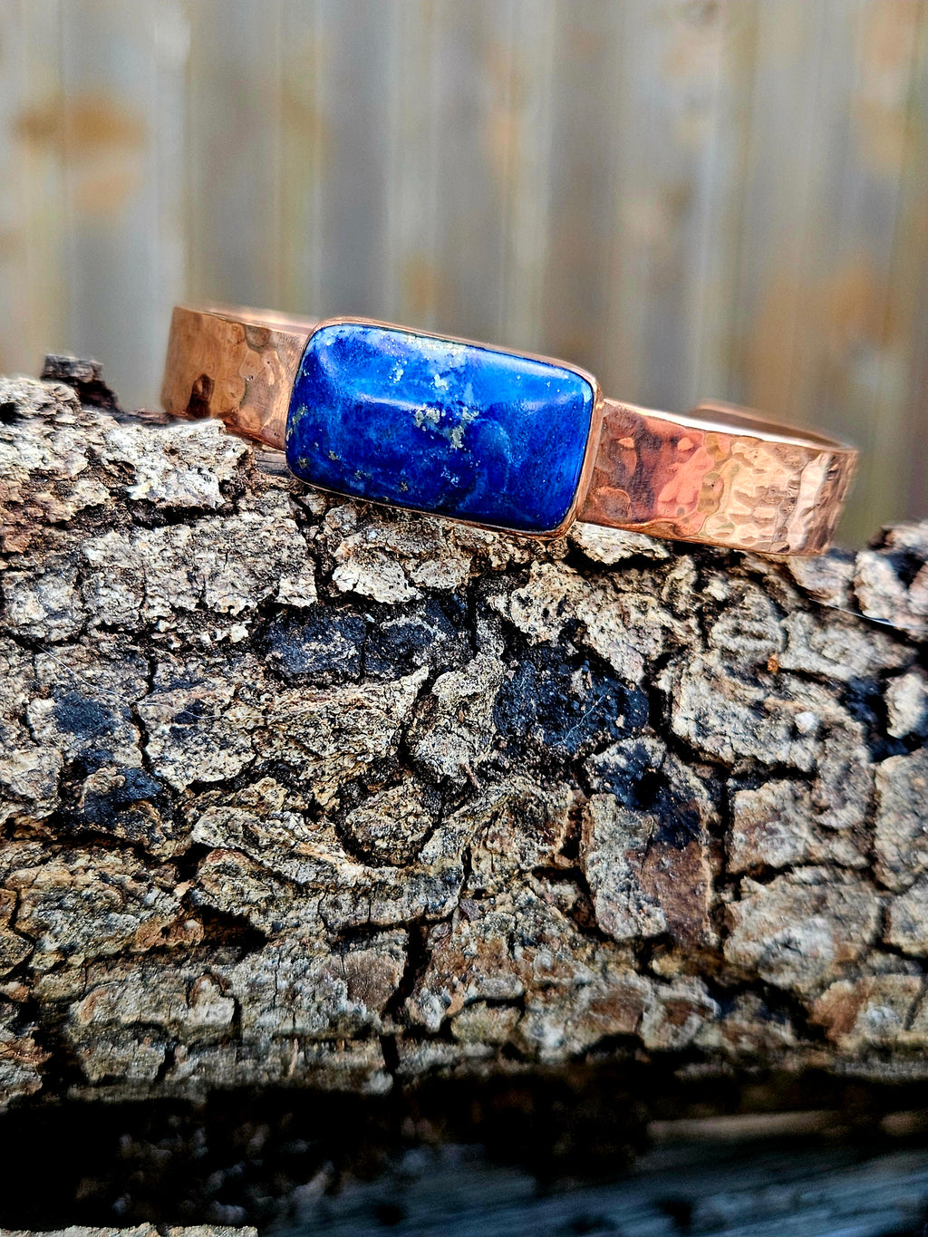 A hammered copper cuff bracelet with a rectangular blue lapis lazuli stone.