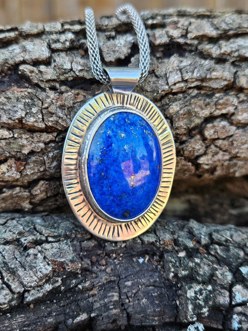 An oval pendant necklace featuring a vibrant blue lapis lazuli stone in a textured silver bezel setting.