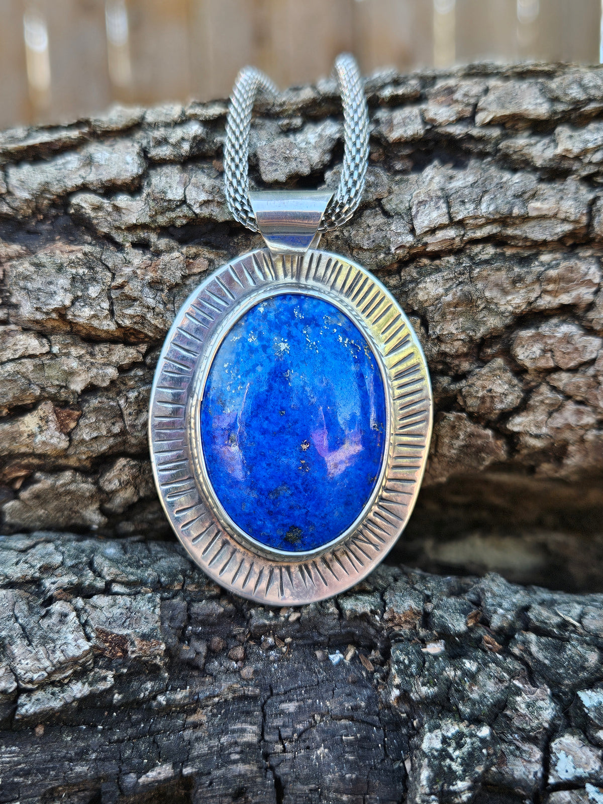 An oval pendant necklace featuring a vibrant blue lapis lazuli stone in a textured silver bezel setting.