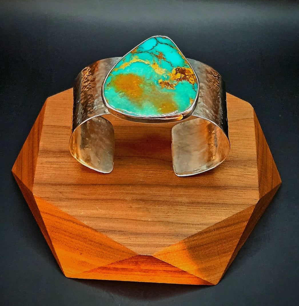 A hammered silver cuff bracelet featuring a large, teardrop-shaped Royston turquoise stone with brown matrix veining.