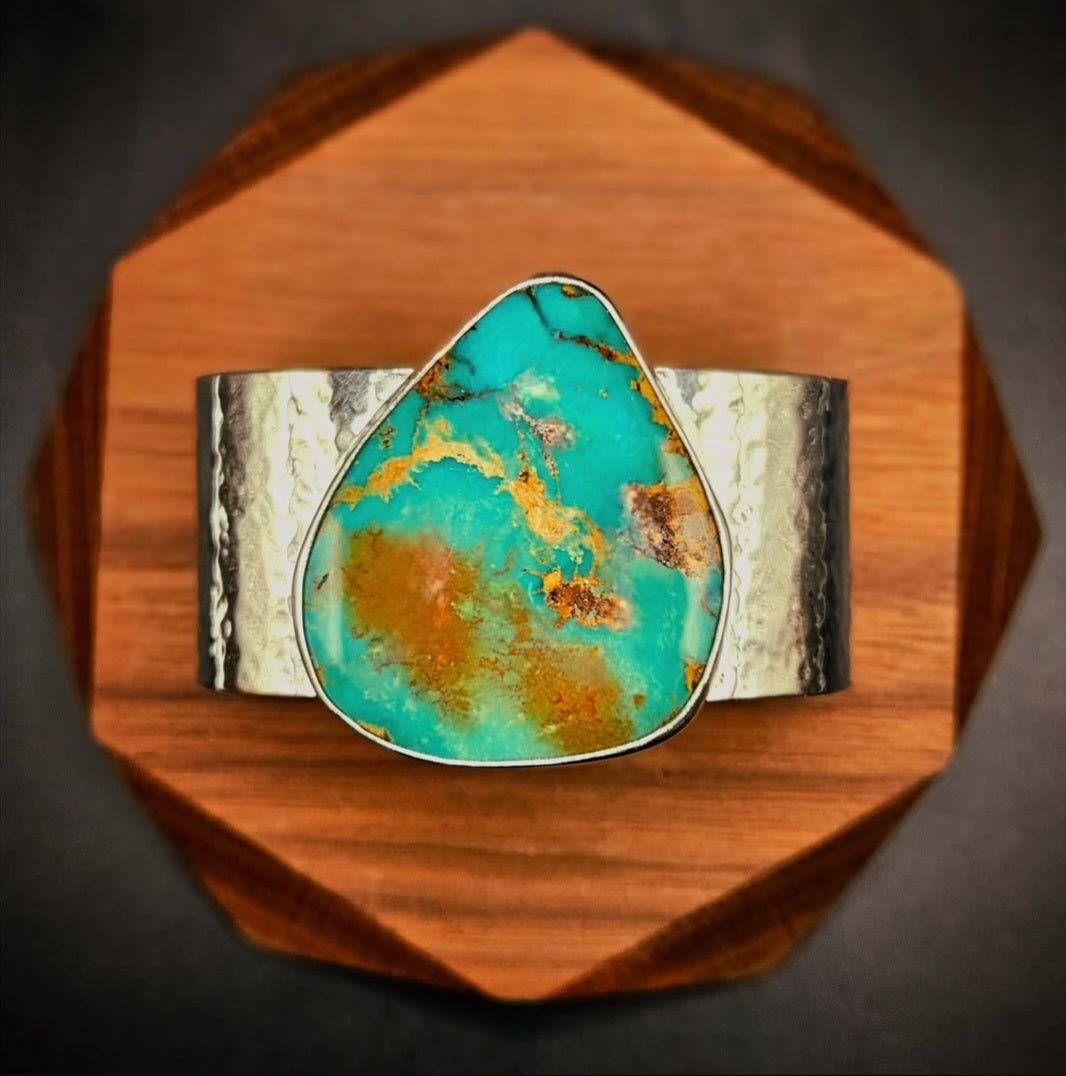 A wide silver hammered cuff bracelet featuring a large, teardrop-shaped Royston turquoise stone with brown and gold matrix patterns. 