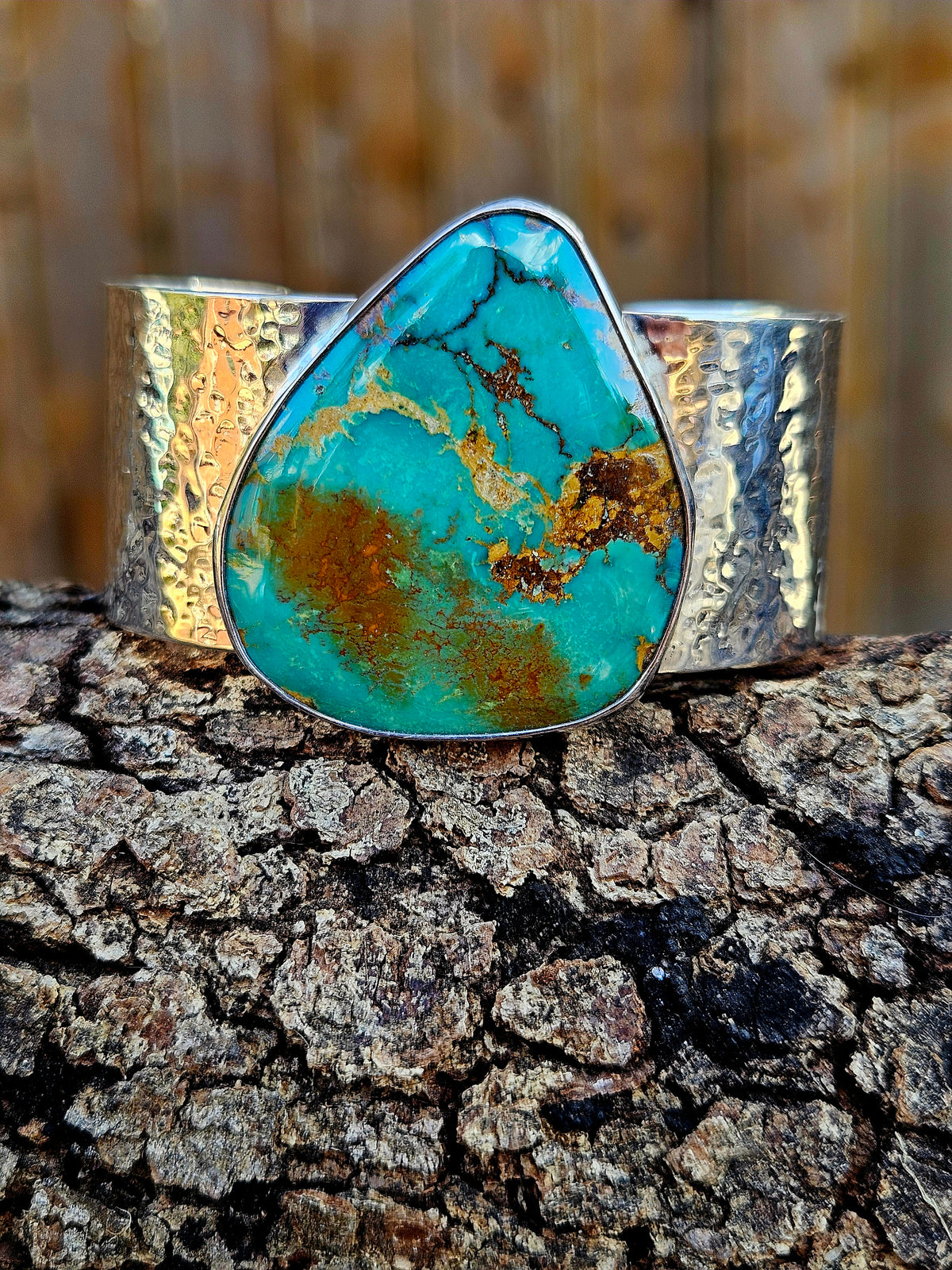 A wide silver hammered cuff bracelet featuring a large, teardrop-shaped Royston turquoise stone with brown and gold matrix patterns. 