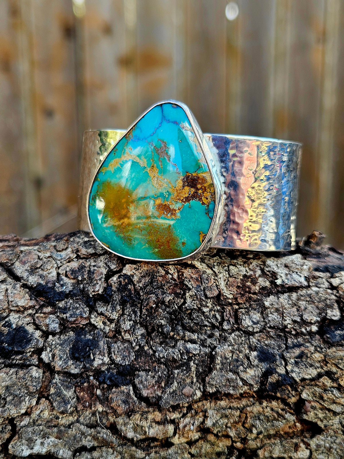 A wide silver hammered cuff bracelet featuring a large, teardrop-shaped Royston turquoise stone with brown and gold matrix patterns. 