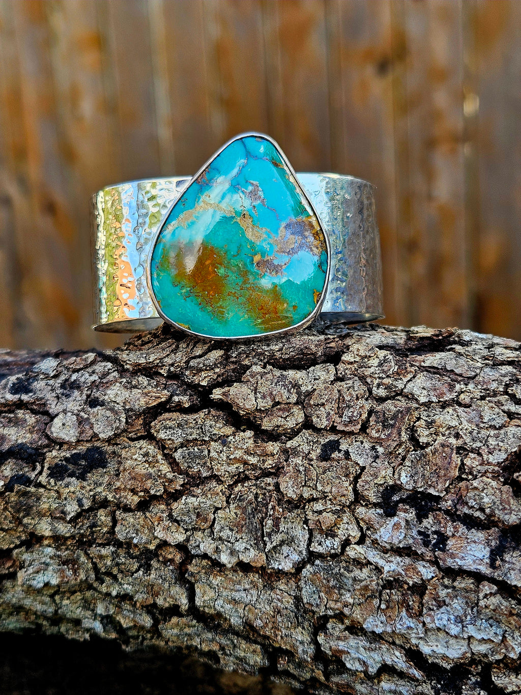 A wide silver hammered cuff bracelet featuring a large, teardrop-shaped Royston turquoise stone with brown and gold matrix patterns. 