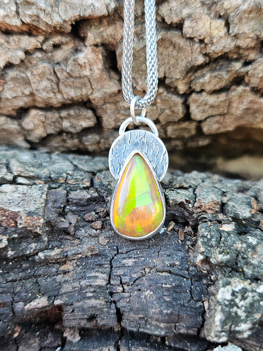 Sterling silver teardrop pendant with amber orange color Ethiopian Opal set on a textured circular backplate. 