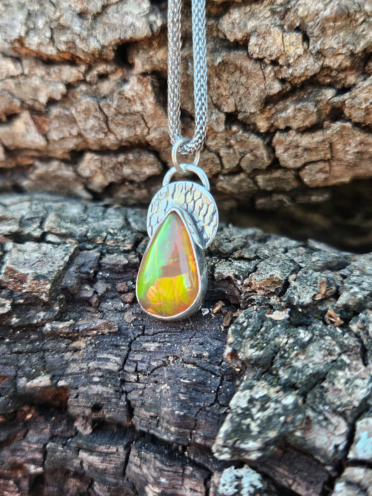 Sterling silver teardrop pendant with amber orange color Ethiopian Opal set on a textured circular backplate. 
