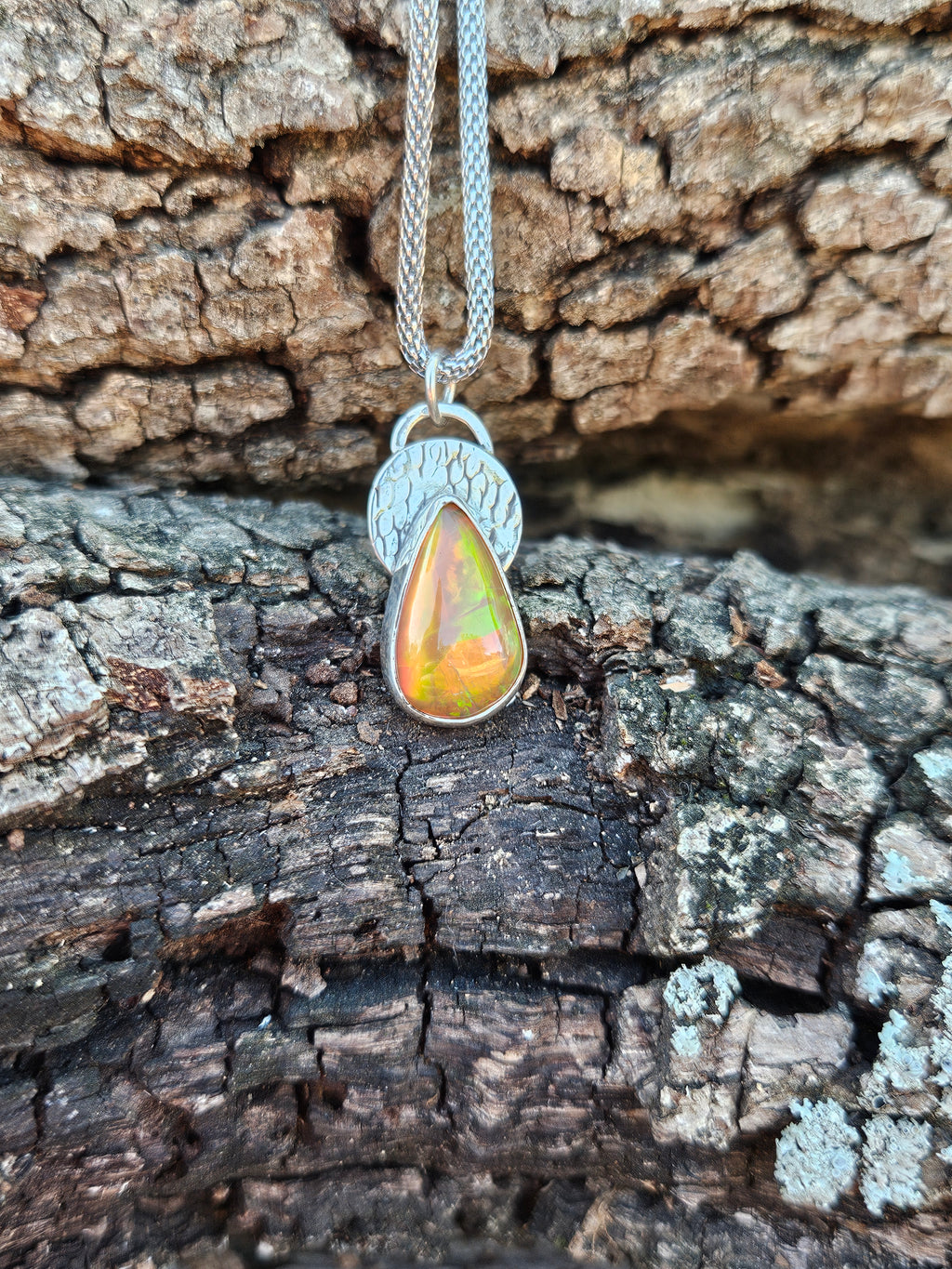 Sterling silver teardrop pendant with amber orange color Ethiopian Opal set on a textured circular backplate. 