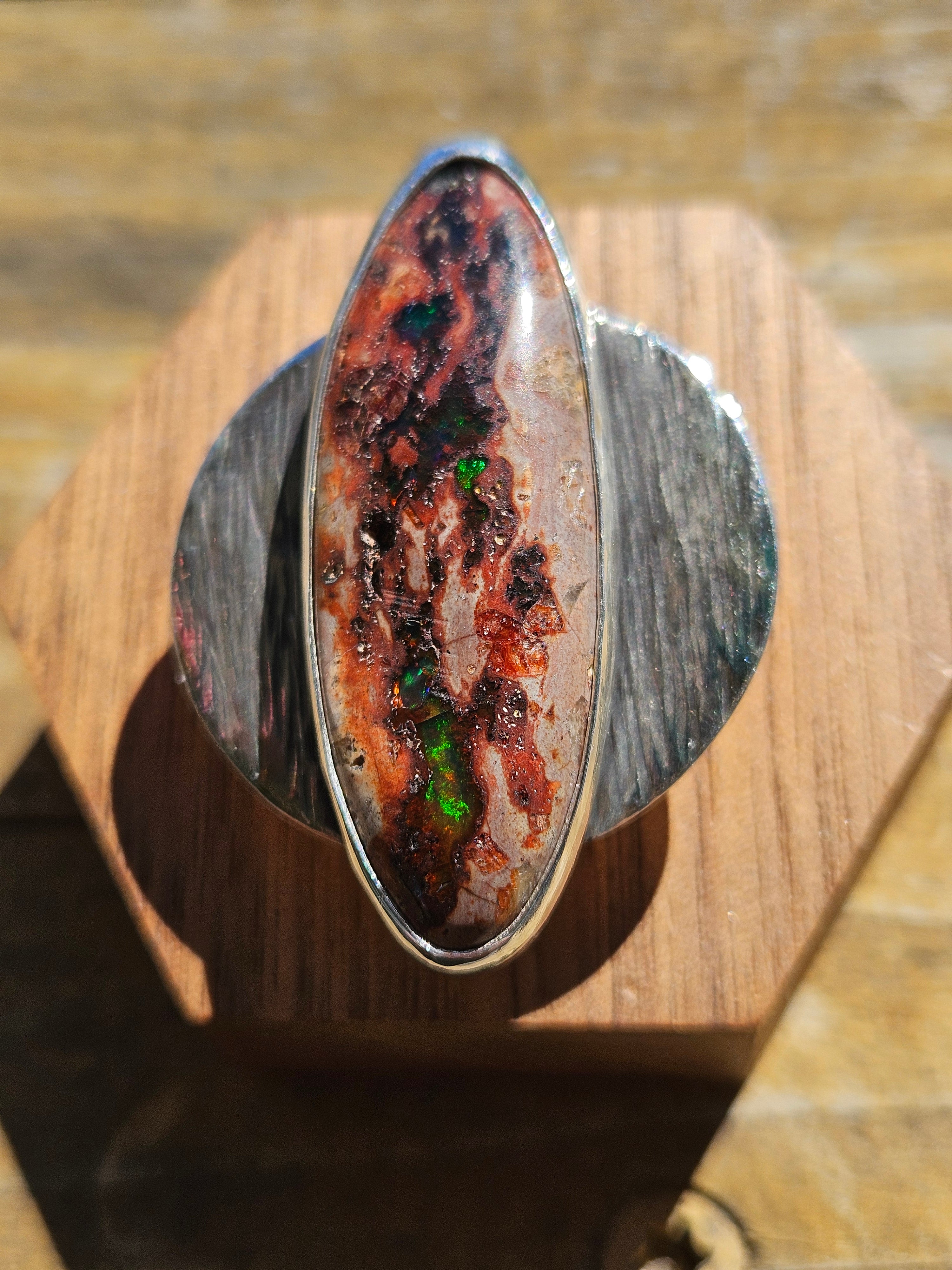 Mexican Matrix Opal Ring in sterling silver with a textured silver backplate. The opals matrix is brown and has pockets of red and green colors. Size 10