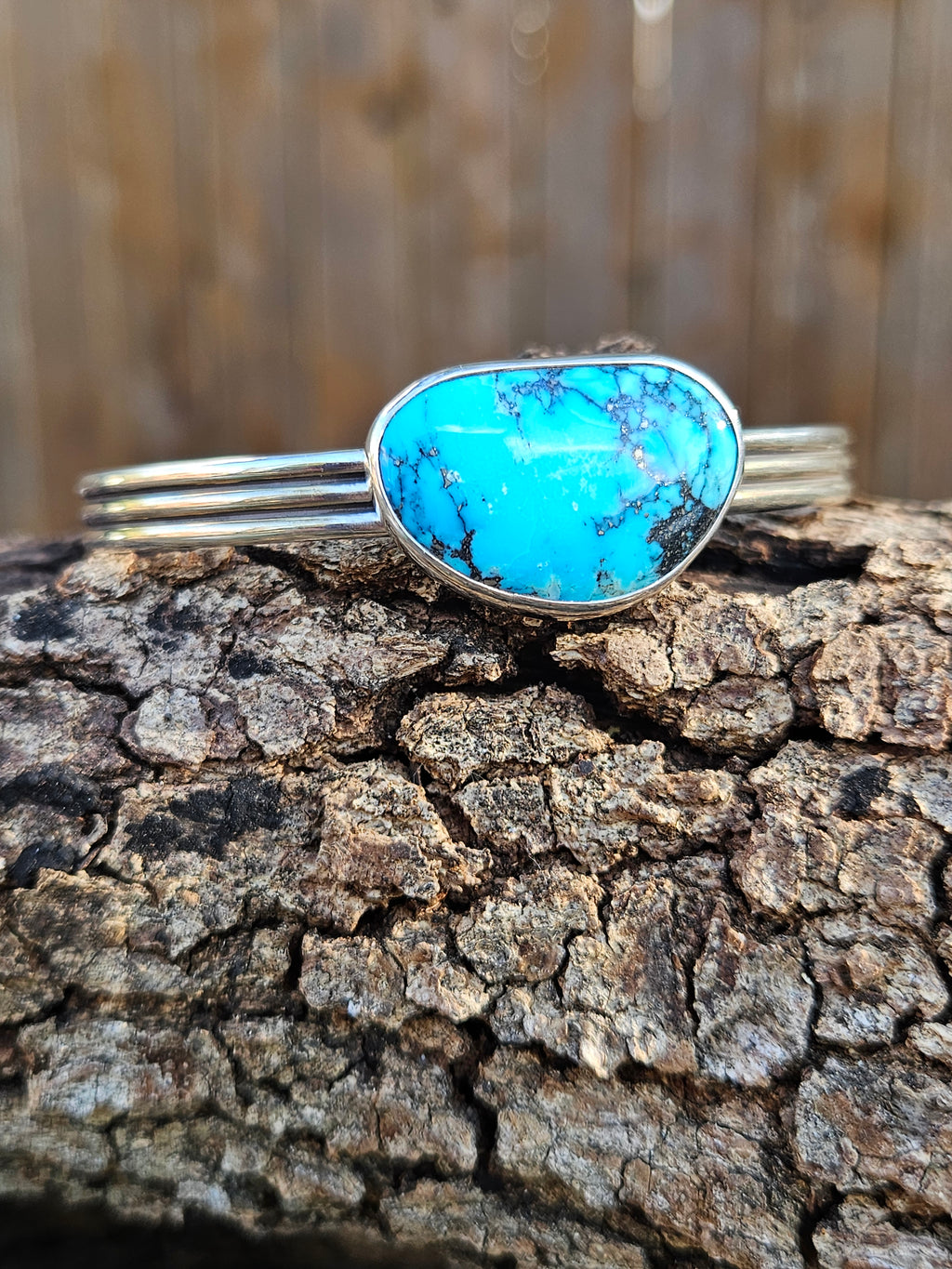 A sterling silver cuff bracelet featuring a large, vibrant turquoise stone with dark matrix veining.