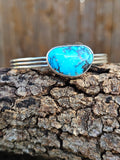 A sterling silver cuff bracelet featuring a large, vibrant turquoise stone with dark matrix veining.