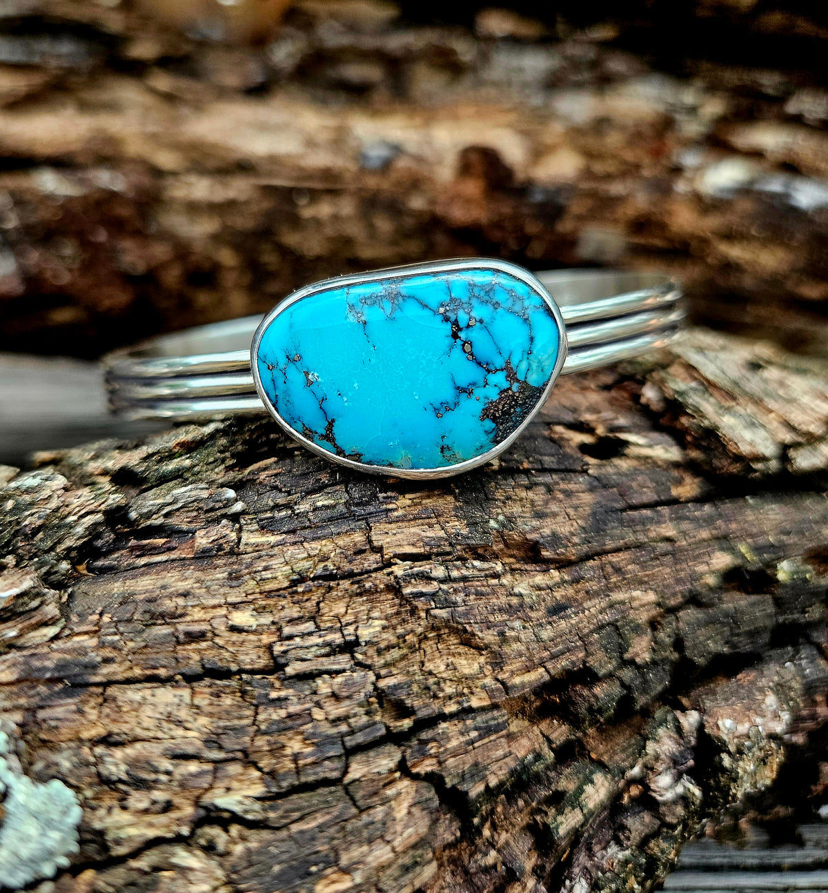 A sterling silver cuff  featuring a large, rounded turquoise stone with black veining.
