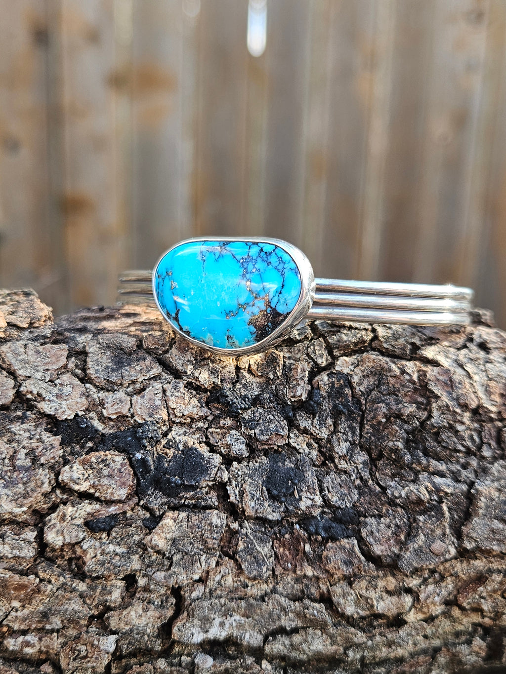 A sterling silver cuff bracelet featuring a large, oval-shaped turquoise stone with dark matrix veining.