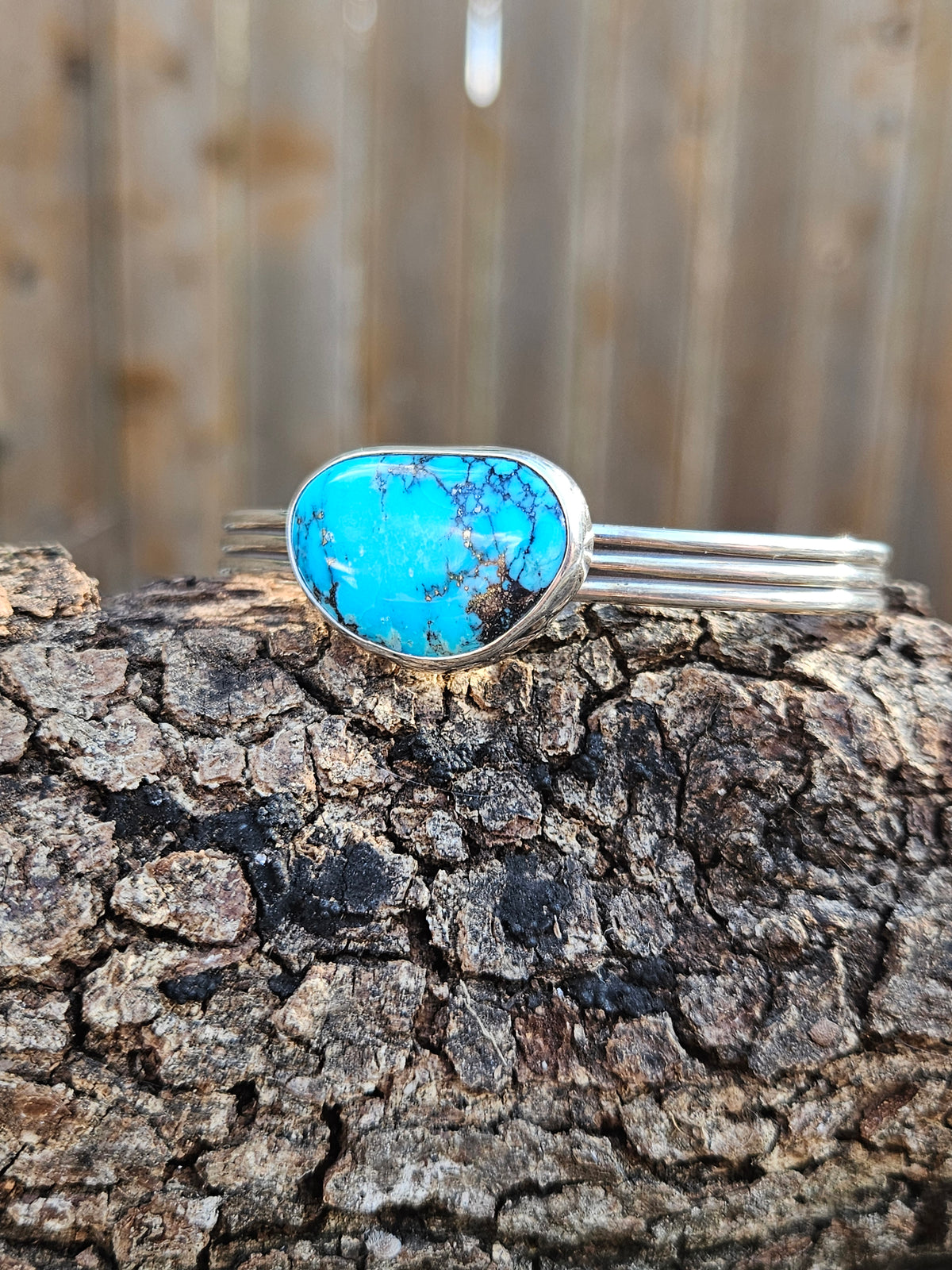 A sterling silver cuff bracelet featuring a large, oval-shaped turquoise stone with dark matrix veining.
