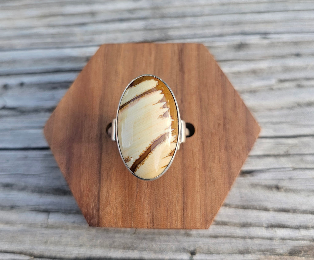 A silver ring with a large oval cabochon featuring a cream and brown striped pattern of picture jasper. 