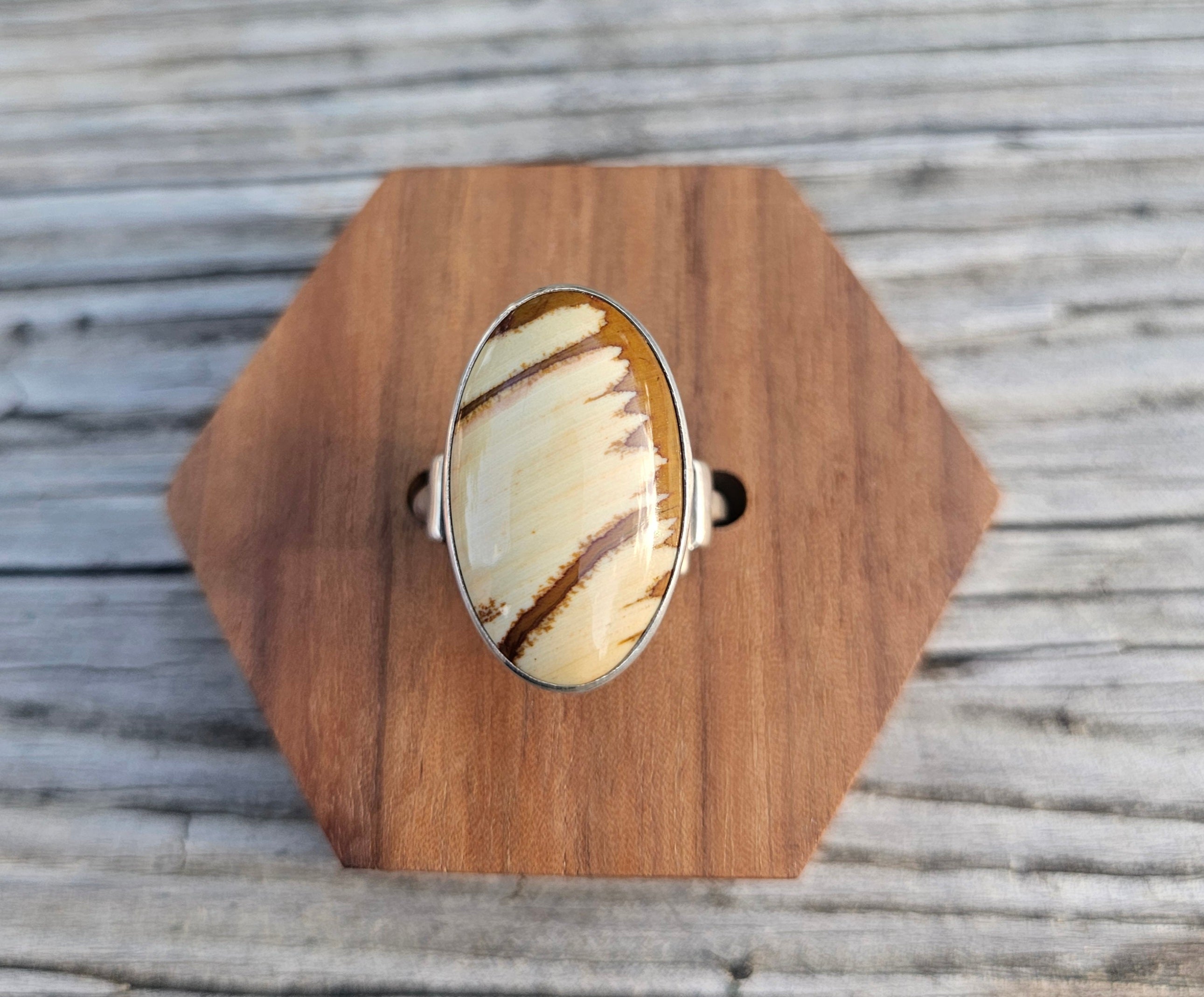 A silver ring with a large oval cabochon featuring a cream and brown striped pattern of picture jasper. 