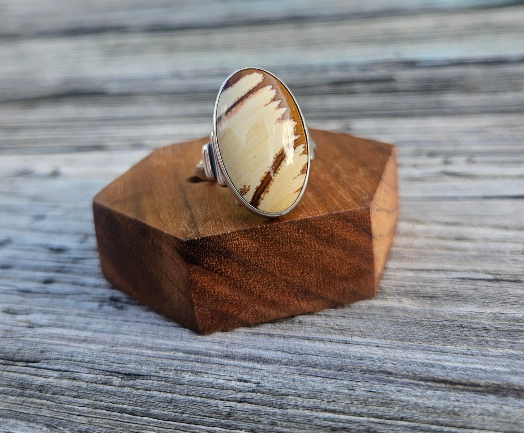 A silver ring with a large oval cabochon featuring a cream and brown striped pattern of picture jasper. 