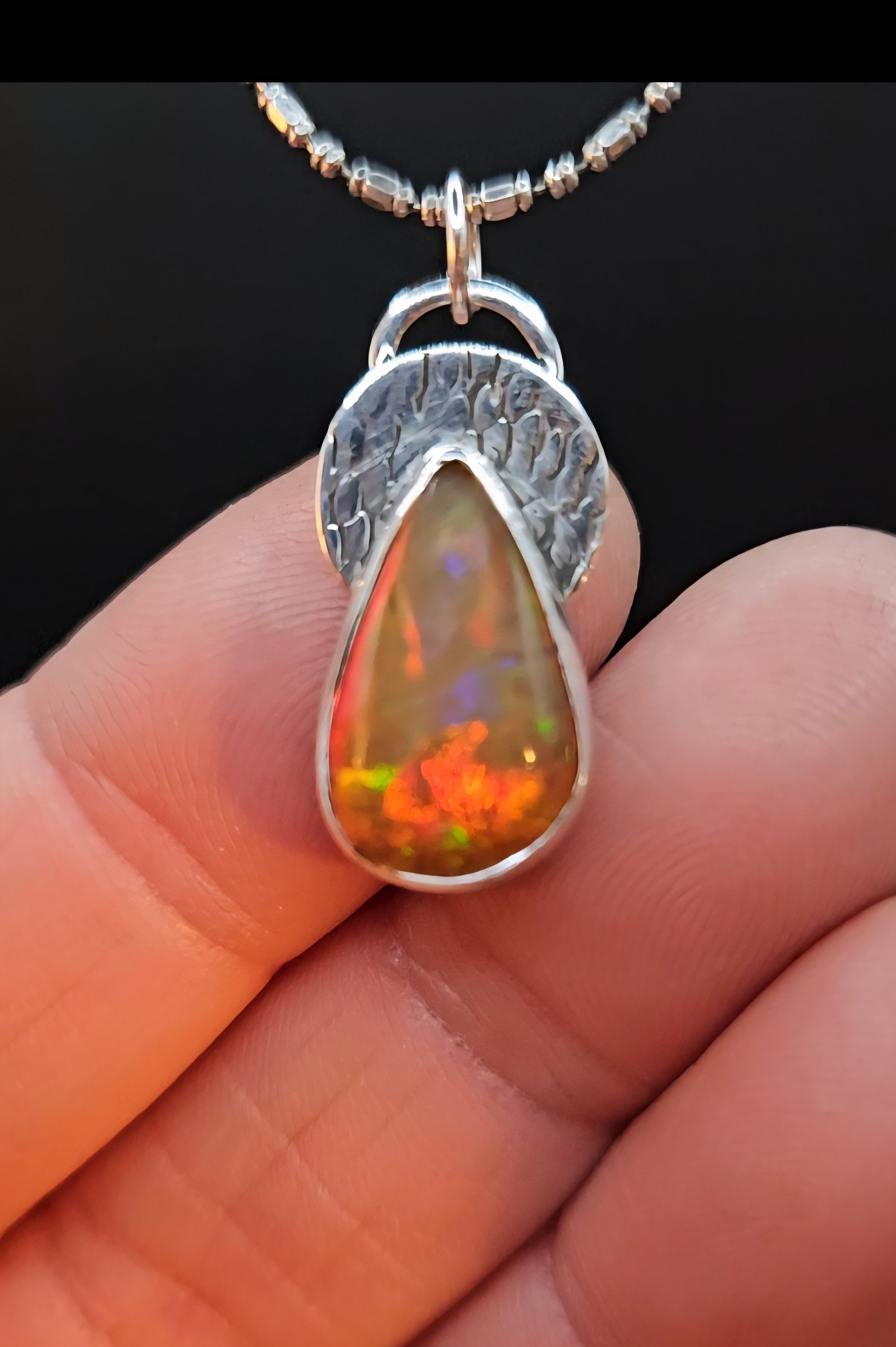 Sterling silver teardrop pendant with amber orange color Ethiopian Opal set on a textured circular backplate. 